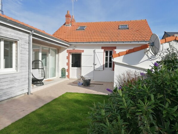 A house with a red-tiled roof, a satellite dish, and a small garden area with grass and plants.