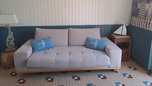 A beige sofa with two blue pillows, a wooden side table, a lamp, and a patterned floor. - Villa pornic 8/9 persons sea view 1min from the beach (Pornic)