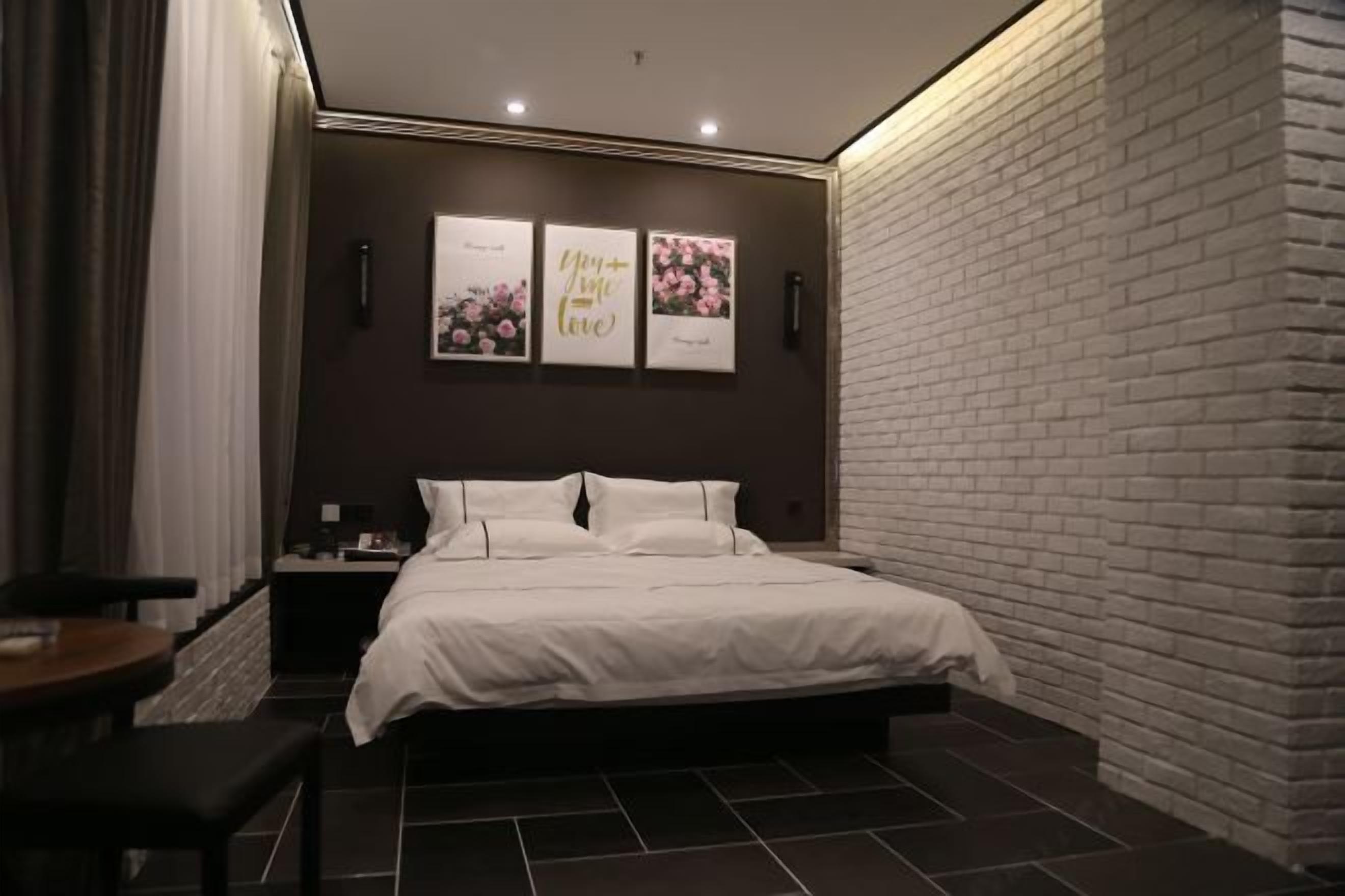 A modern bedroom with a brick accent wall, a large bed, a bedside table, and a wall-mounted artwork.