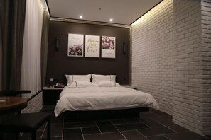 Une chambre à coucher moderne avec un mur d’accent en briques, un grand lit, une table de chevet et une œuvre d’art accrochée au mur.