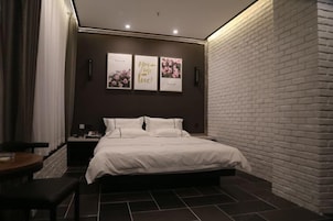 Un dormitorio moderno con una pared de ladrillo decorativa, una cama grande, una mesita de noche y una obra de arte colgada en la pared.