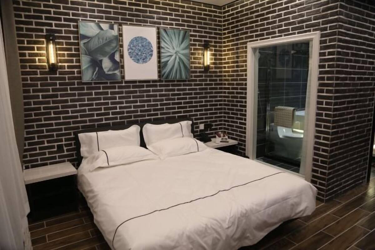A modern bedroom with a brick-patterned wall, a large bed with white bedding, and two wall-mounted light fixtures.