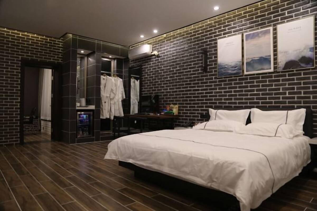 A modern hotel room with a brick wall, a large bed, a wardrobe, and a mirror.
