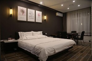 A modern hotel room with a large bed, bedside tables, a desk, and a chair. There are wall-mounted lights and a large window with curtains. - Shou Cheng Hotel Select (Mishan)