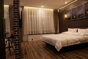 Habitación de hotel con una cama grande, un escritorio, una silla, un ventanal con cortinas y una pared de ladrillo.