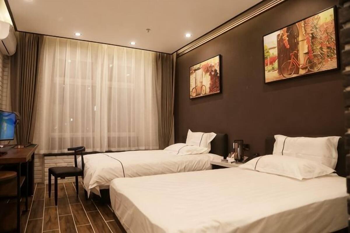 A hotel room with two beds, a desk, a chair, a TV, and artwork on the walls.