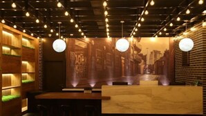 A modern bar area with a wooden reception desk, bar stools, and a mural of a city street. - Shou Cheng Hotel Select (Mishan)