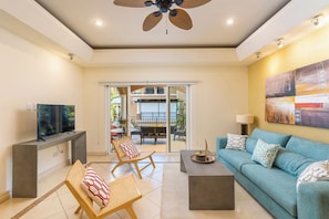 A living room with a sofa, chairs, a coffee table, a TV, and a ceiling fan.