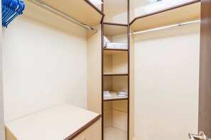 A walk-in closet with multiple shelves and hanging space, featuring a metal rod and a wooden door.