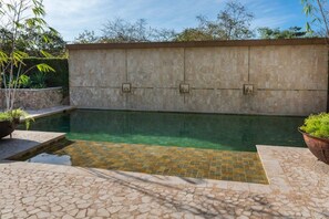 Une piscine dont le bord est revêtu de pierres, entourée d’un petit muret en pierre et agrémentée de plantes en pot.