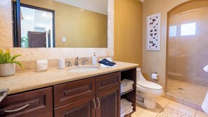 Een badkamer met een wastafel, spiegel, handdoekhouder, toilet, douche en decoratief wandobject.
