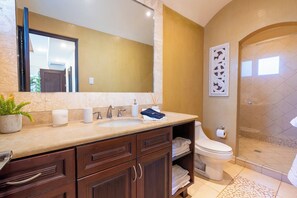 Une salle de bain comprenant un lavabo, un miroir, un porte-serviettes, des toilettes, une douche et un élément décoratif mural.