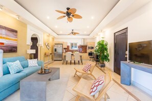 Un salon moderne comprenant un canapé, des fauteuils, une table basse, un téléviseur et un ventilateur de plafond.