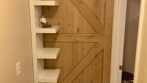 A wooden door with a diagonal brace design, flanked by white shelving units with a small decorative item on the top shelf.