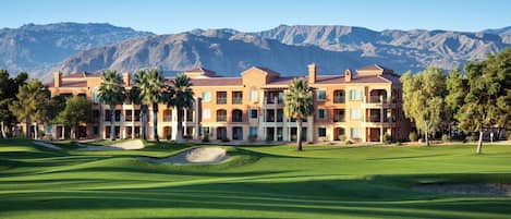 Un hotel con un campo de golf frente a él, que cuenta con un edificio grande con varios balcones y palmeras.