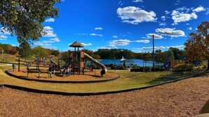 A playground with slides and climbing structures, surrounded by a lake and trees.