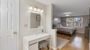 A bedroom with a bed, a bedside table, a dresser, a mirror, and a window with blinds.