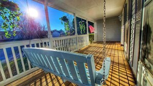 A porch with a swing, white railings, and a view of the outdoors.