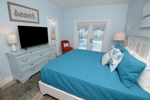 A bedroom with a bed, a television, a dresser, a red chair, and a door with a view.