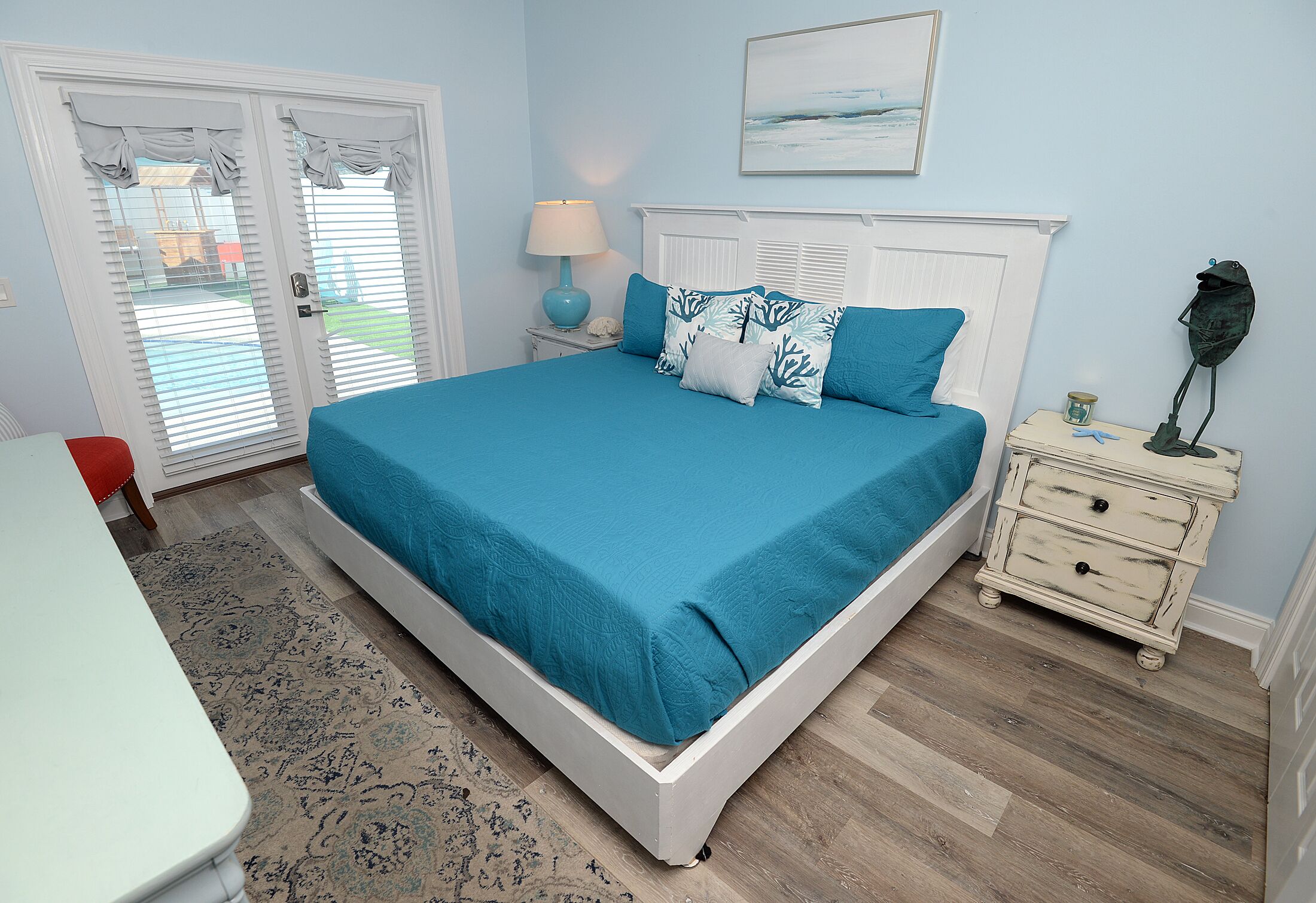 A bedroom with a bed, a nightstand, a lamp, a dresser, and a door with shutters.