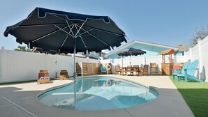 Un patio trasero con piscina, sillas de descanso y sombrillas.