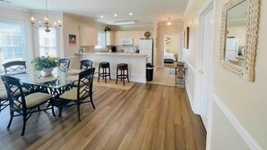 A spacious kitchen with a central island, wooden flooring, and a dining area with a glass table and chairs.