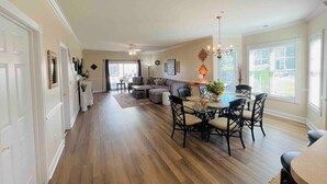 A spacious living area with a dining table and chairs, a sofa, and a kitchen in the background.