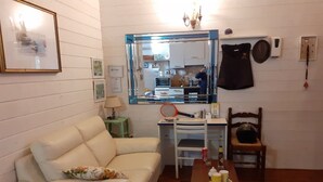 A living room with a white sofa, a small table with a cup and a bottle, a mirror above a desk, and a kitchen visible through the mirror.