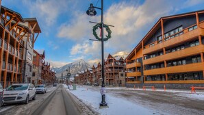 Eine verschneite Straße mit mehrstöckigen Gebäuden, darunter ein Hotel mit Balkonen, vor einer Bergkulisse.