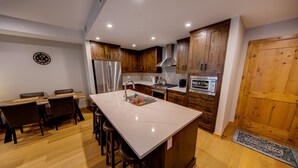 Eine moderne Küche mit Holzschränken, einem Edelstahlkühlschrank, einer Kochinsel mit Hockern und einer Mikrowelle.