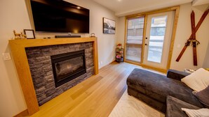 Ein Wohnzimmer mit Kamin, Flachbildfernseher, einer Couch und einer Glastür.