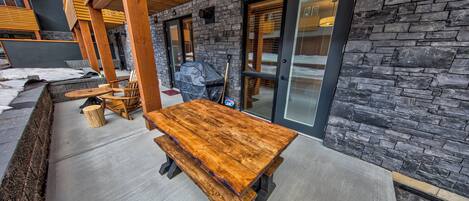 Un patio al aire libre con mesas y bancos de madera, muros de piedra y una parrilla cubierta.