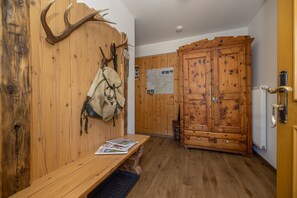 A wooden cabin interior with a bench, a coat rack with a backpack, a large wooden cabinet, and a map on the wall.