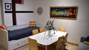 Un espace de vie compact comprenant un lit, une table à manger avec des chaises, une horloge et un tableau abstrait aux couleurs vives accroché au mur.