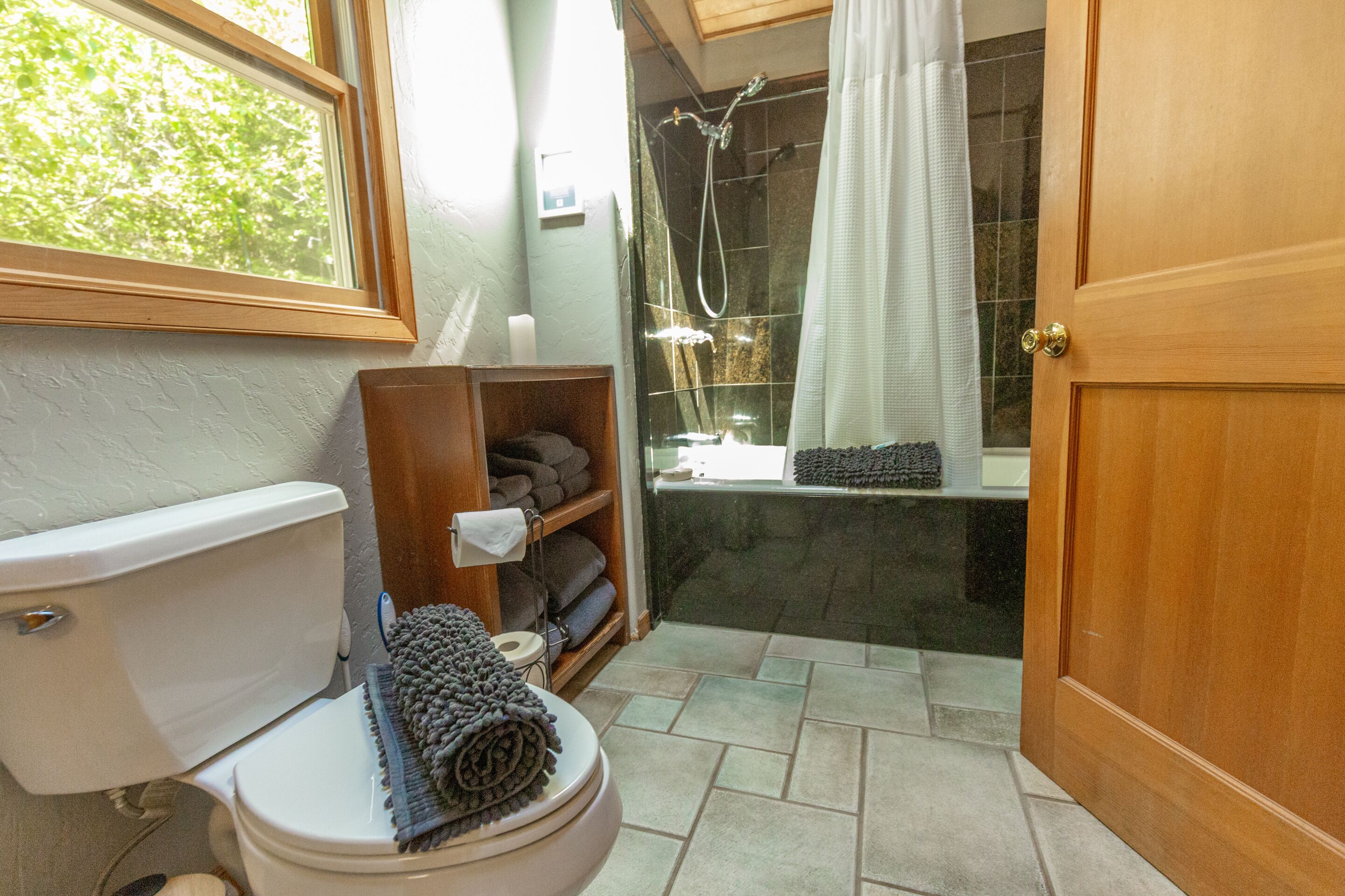 Une salle de bain avec des toilettes, une douche et une étagère en bois où sont posées des serviettes.