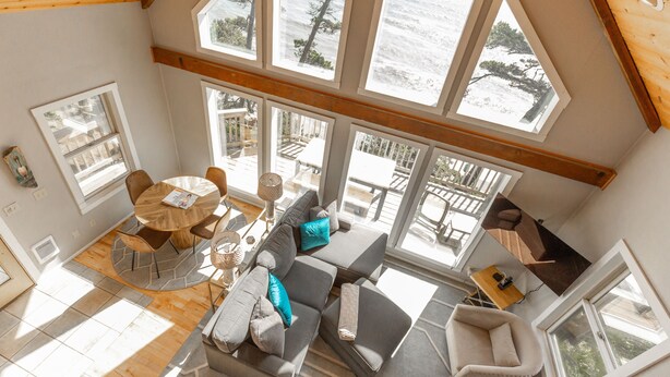 A spacious room with a large window overlooking the sea, a cozy seating area with a sofa and chairs, and a dining table with chairs. - Honeymoon Cove at Crook Point (Brookings)