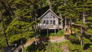 A cabin surrounded by dense forest, with a deck and outdoor seating area. - Honeymoon Cove at Crook Point (Brookings)