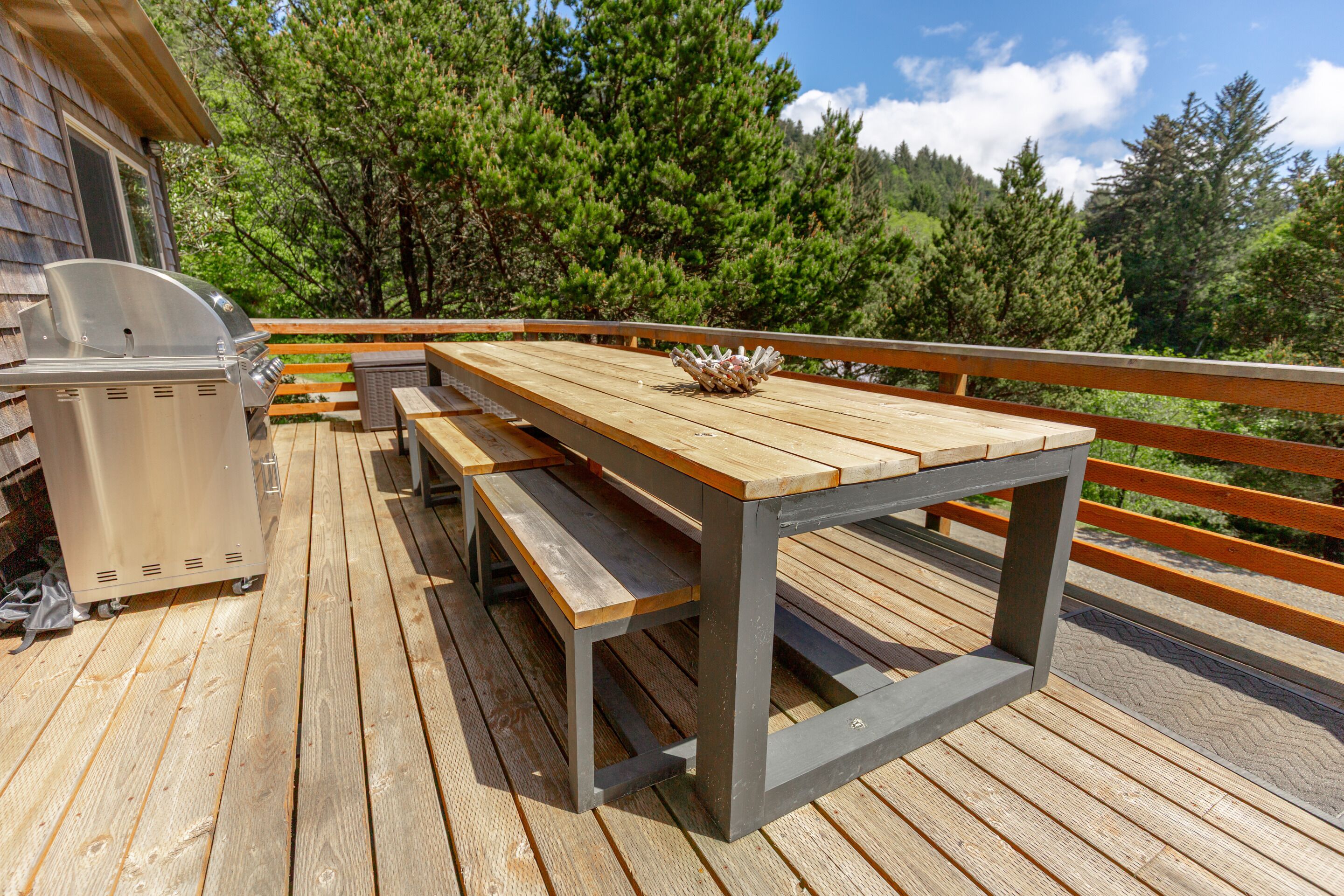 Een houten terras met een barbecue, picknicktafel en bankjes.