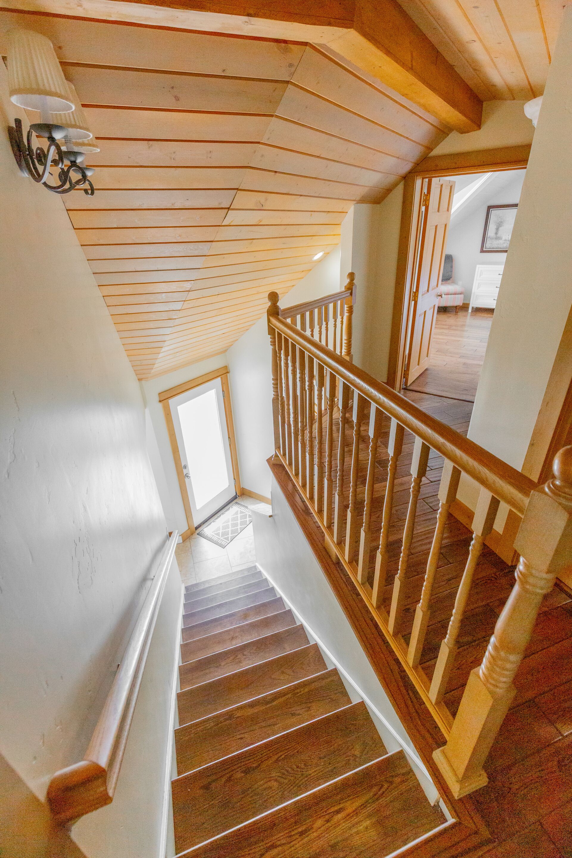 Un escalier en bois, doté d’une rampe, mène à une pièce qui possède une porte et une fenêtre.
