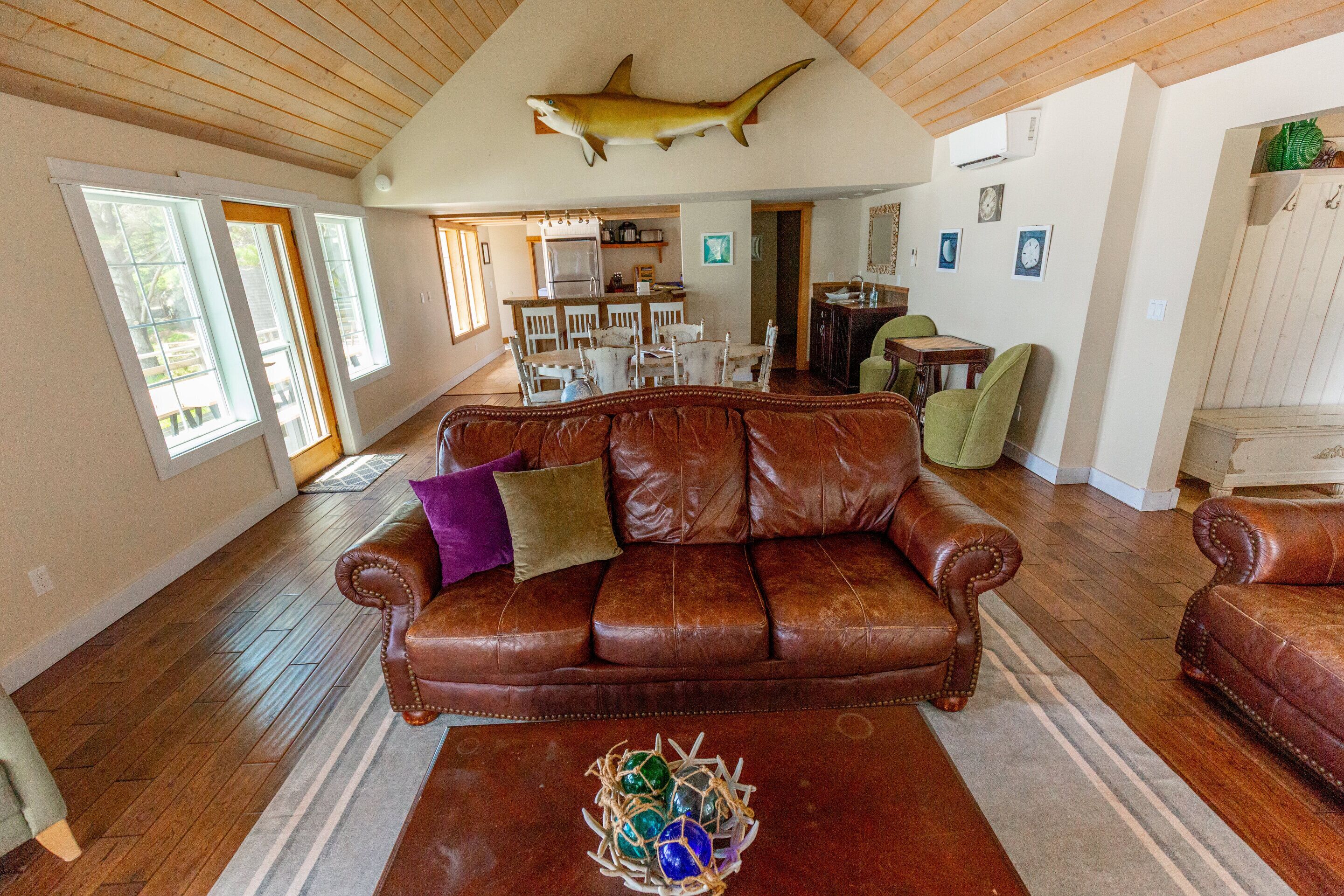 A spacious living room with a brown leather sofa, a coffee table with decorative glass balls, and a ceiling-mounted shark decoration.