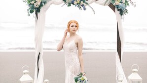 Ein Strandhochzeitsaufbau mit einem weißen Bogen, verziert mit Blumen und Laternen.
