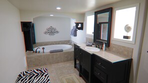 A modern bathroom with a bathtub, two sinks, a large mirror, and a decorative wall piece.