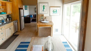 A modern kitchen with wooden cabinets, a stainless steel refrigerator, and a dining area with a table and chairs. - Beach Bungalow at Crook Point (Brookings)