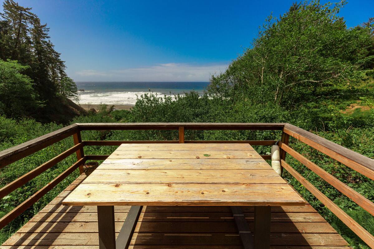 A wooden deck with a bench overlooking a beach and ocean.