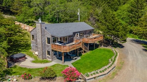 A modern two-story house with a deck, surrounded by lush greenery and a dirt road. - Beach Bungalow at Crook Point (Brookings)