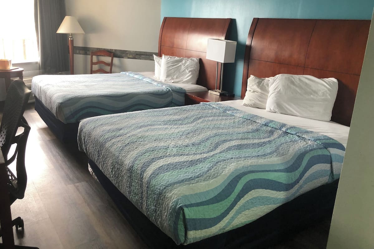 A hotel room with two beds, each with a blue and white patterned bedspread, wooden headboards, and white pillows.