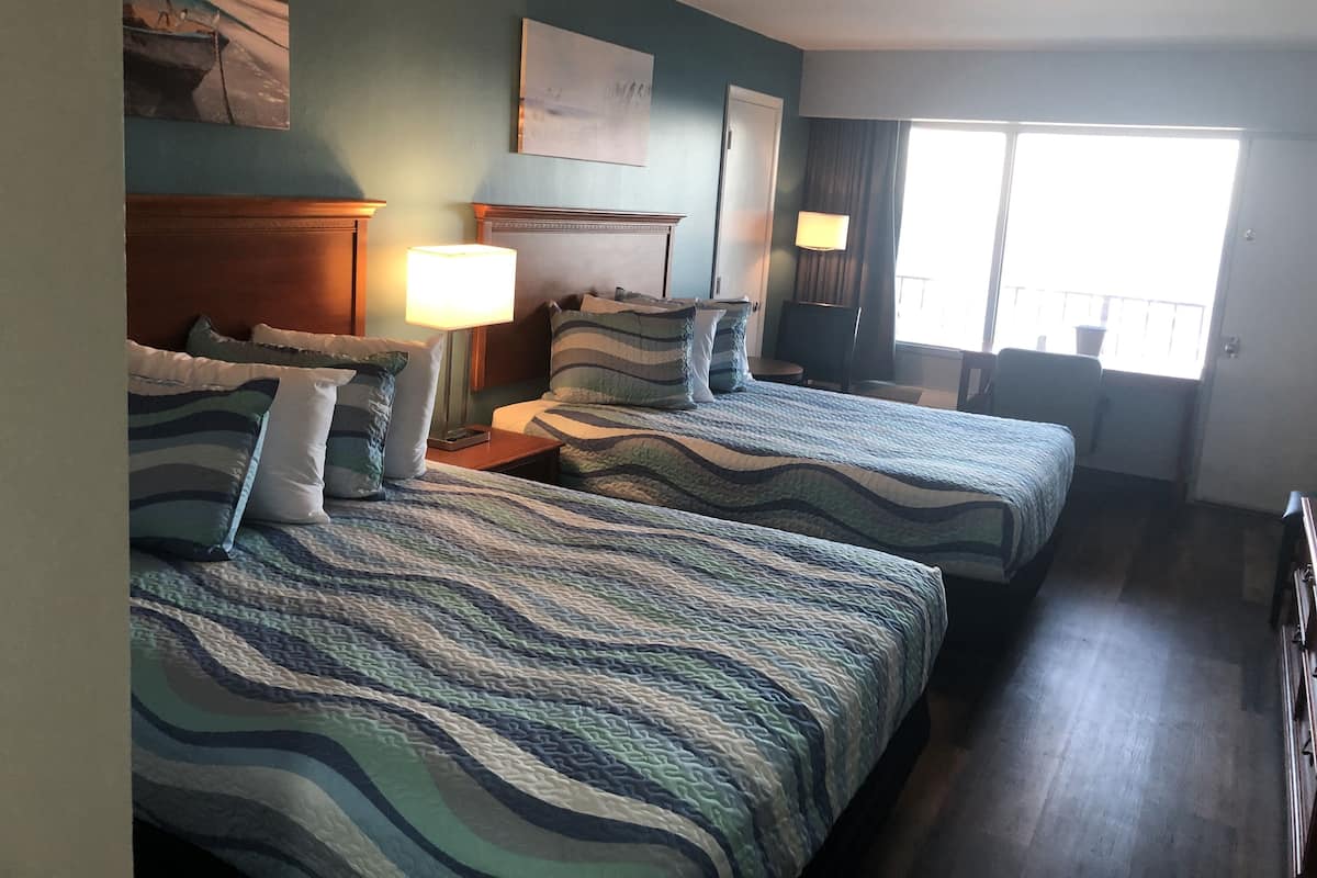 A hotel room with two beds, a nightstand, a lamp, a painting, and a window with curtains.