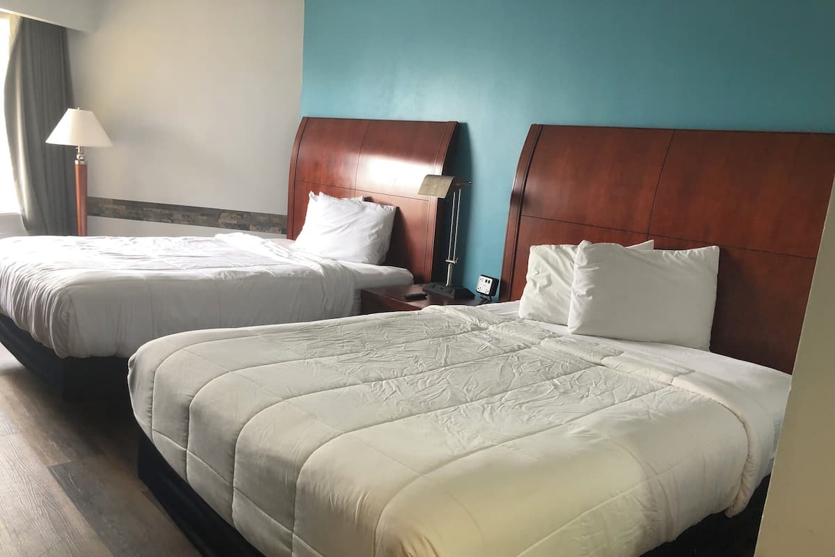 A hotel room with two beds, each with white bedding and wooden headboards.