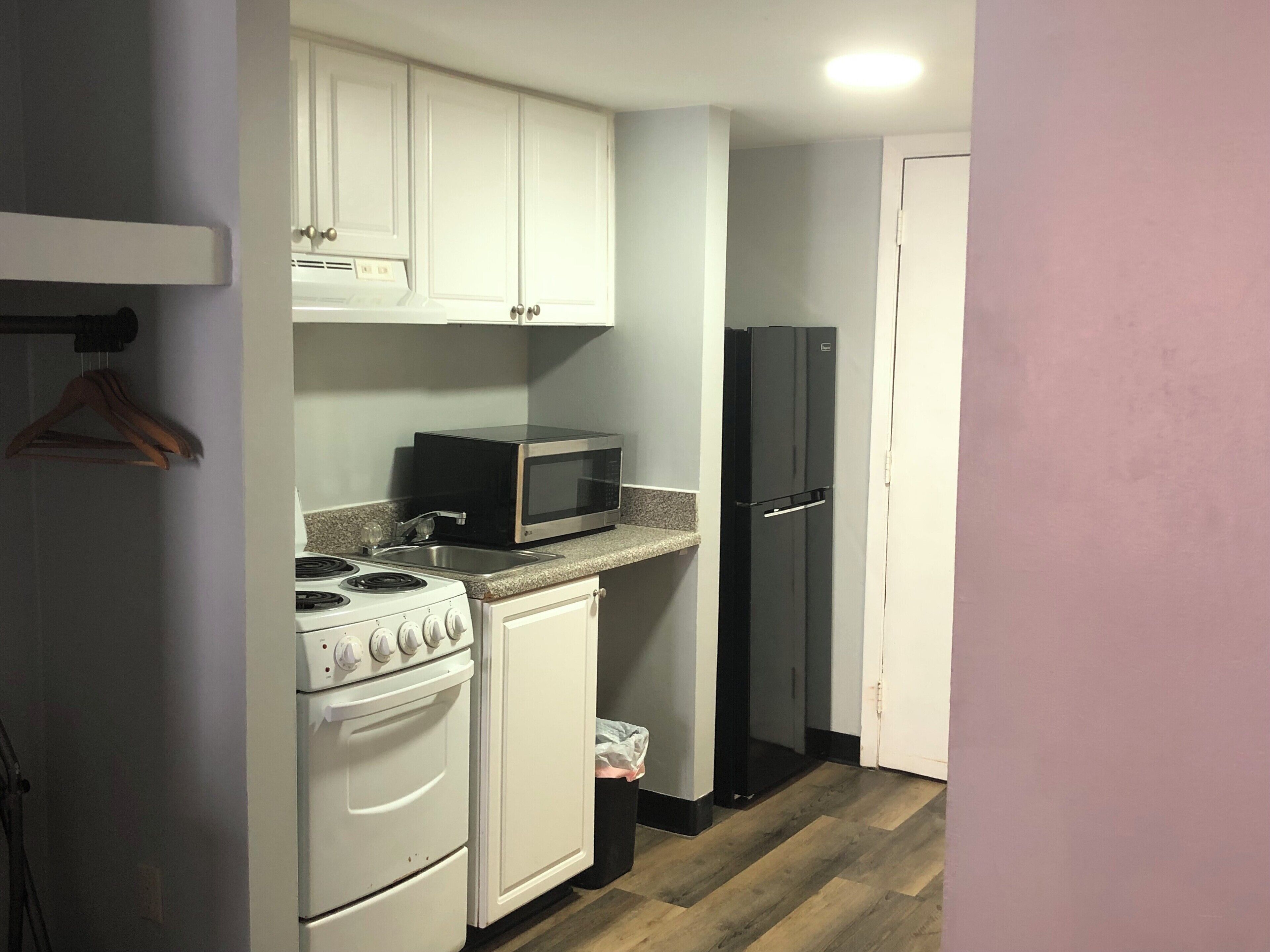 Una cocina compacta con gabinetes blancos, una estufa, un microondas y un refrigerador negro.