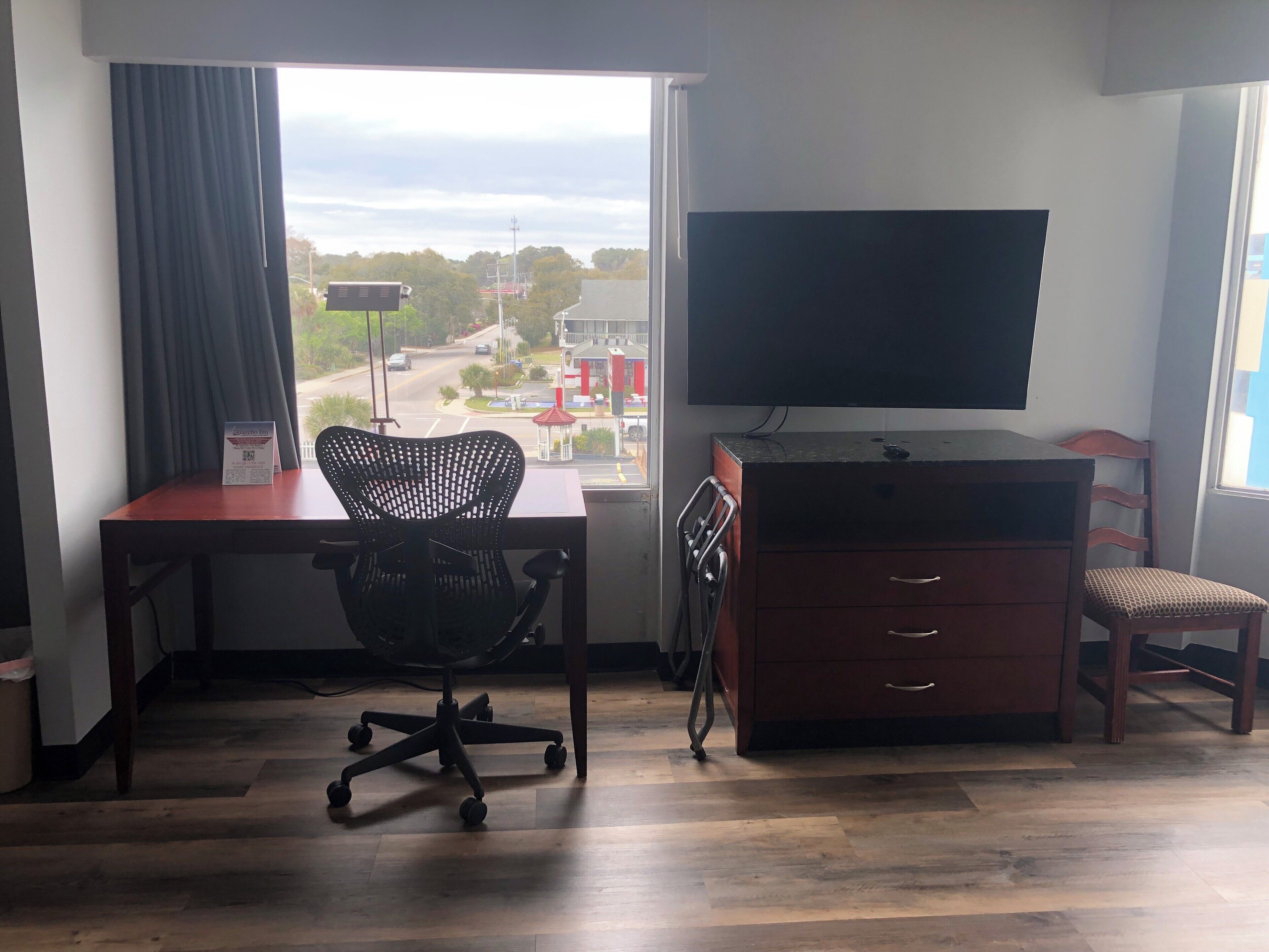 Una habitación con escritorio, silla de oficina, televisor y un pequeño armario de madera.